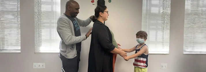 Dr. Cooley examining a pregnant patient's back while she holds hands with her son